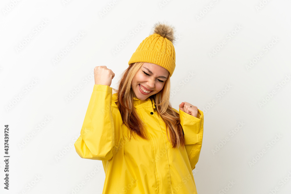 Teenager blonde girl wearing a rainproof coat over isolated white background celebrating a victory Teenager blonde girl wearing a rainproof coat over isolated white background celebrating a victory