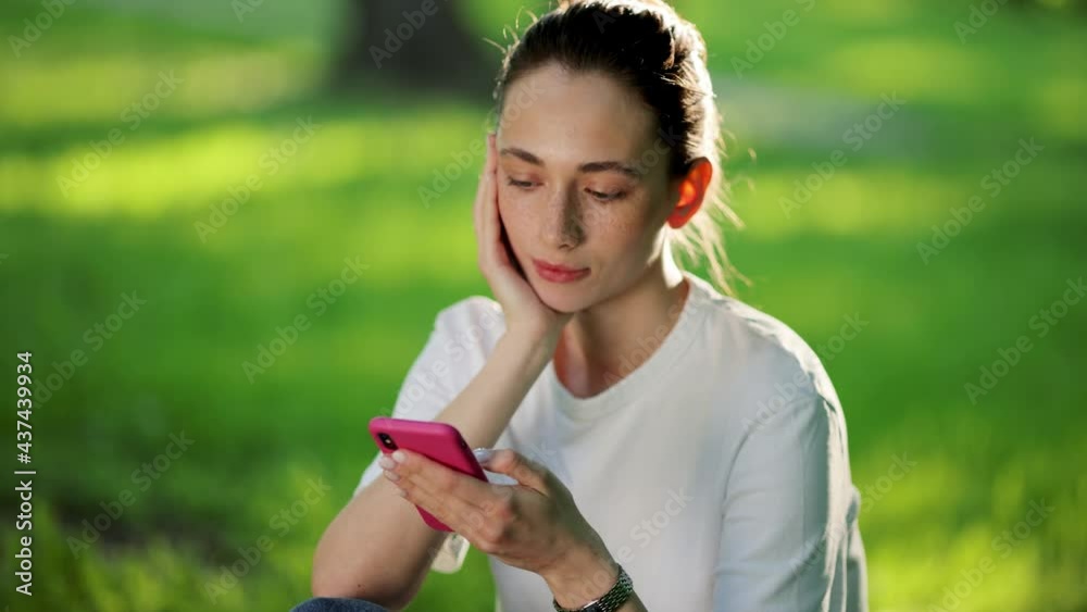 Beautiful smiling woman with nice Freckles sitting on the grass on a summer day and using a mobile phone. digital nomad summer lifestyle on the go Beautiful smiling woman with nice Freckles sitting on the grass on a summer day and using a mobile phone. digital nomad summer lifestyle on the go