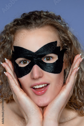 Cheerful and surprised girl in a black cosmetic skincare mask that eliminates bags under the eyes