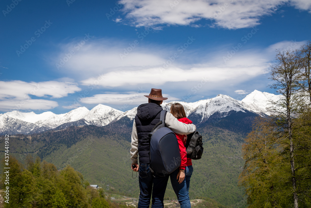 A man and a woman look at the snow-capped peaks of the mountains