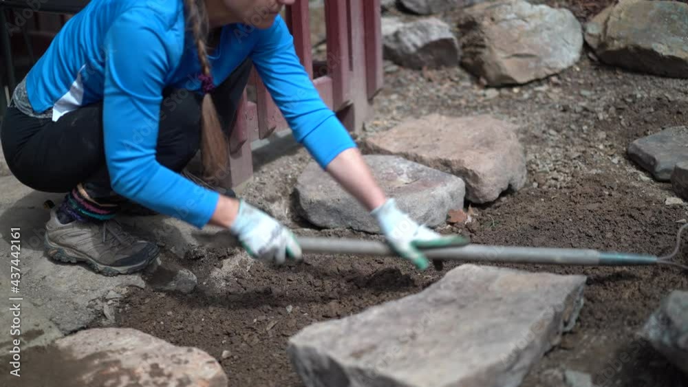 Mature woman rakes area for hardscaping with large rocks. Mature woman rakes area for hardscaping with large rocks.