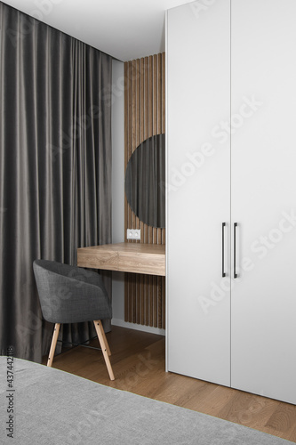 Elegant mirror on wooden frame wall above minimal wood console table in trendy bedroom interior of grey tones