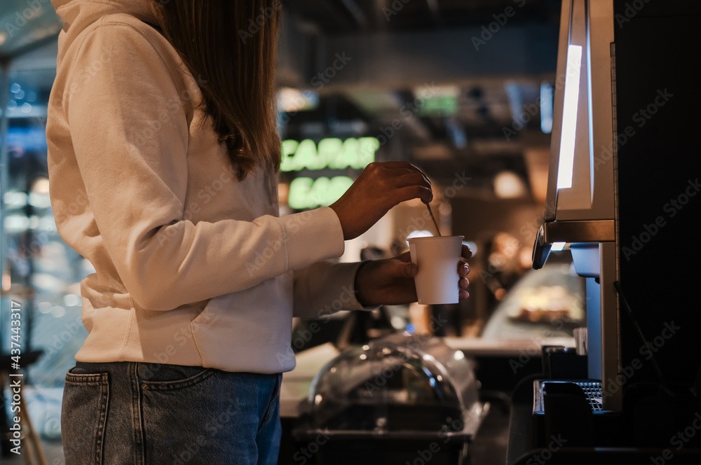 young woman prepares herself coffee through a self-service coffee machine in a cafe. woman near the coffee maker makes cappuccino
