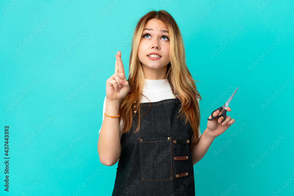 Obraz premium Young hairdresser girl over isolated blue background with fingers crossing and wishing the best