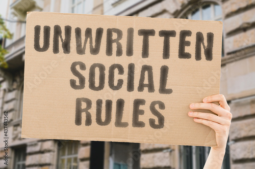 The phrase " Unwritten social rules " on a banner in men's hand. Human holds a cardboard with an inscription. Friendship. Communication. Communicate. Relationship. Social issues © AndriiKoval