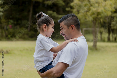 Hispanic dad hugging his little daughter in the park-father and daughter outdoors smiling face to face