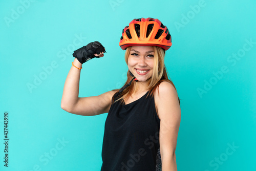 Young cyclist girl over isolated blue background doing strong gesture © luismolinero