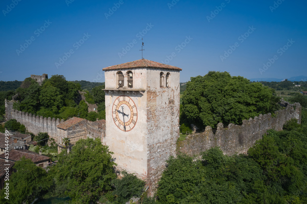 Aerial view of the Italian historic castle Castello di Monzambano on the hill. Monzambano Castle, Italy. Old clock on the tower of the castle. Aerial view of the Italian historic castle Castello di Monzambano on the hill. Monzambano Castle, Italy. Old clock on the tower of the castle.