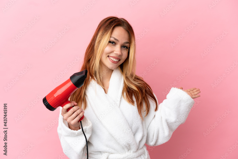 Teenager blonde girl holding a hairdryer over isolated pink background extending hands to the side for inviting to come Teenager blonde girl holding a hairdryer over isolated pink background extending hands to the side for inviting to come