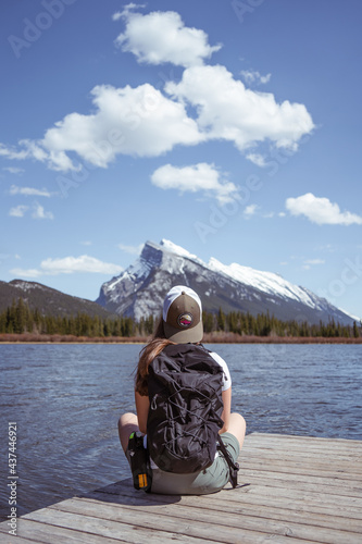 Hiker girl sitting on a wooden pier at Vermillion Lakes in Banff National Park with the snowy Rundle Mountain Range in the background