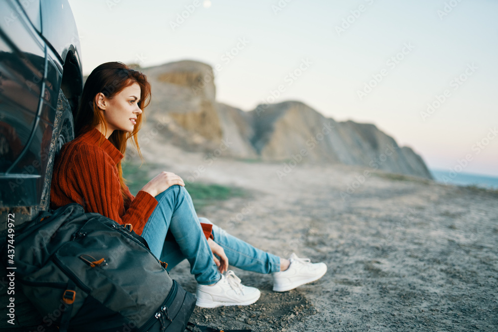woman in jeans and sneakers sits on the sand near the car in nature woman in jeans and sneakers sits on the sand near the car in nature