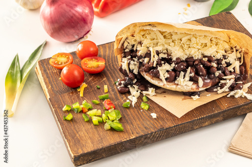 Venezuelan domino arepa with black beans and lots of grated cheese on wooden board and fresh kitchen seasonings