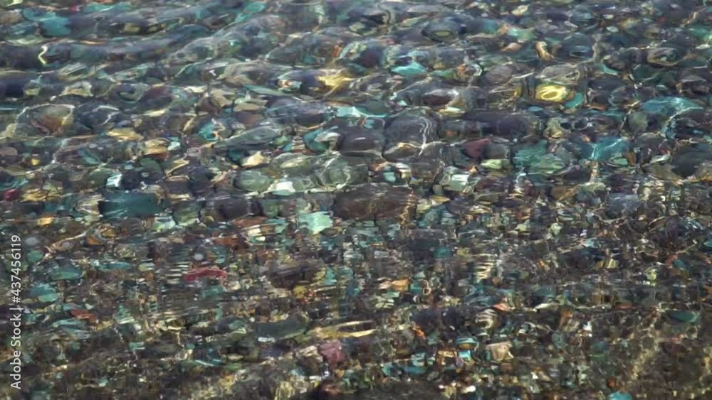 Shiny multi colored pebbles inside clean sea in slow motion Shiny multi colored pebbles inside clean sea in slow motion