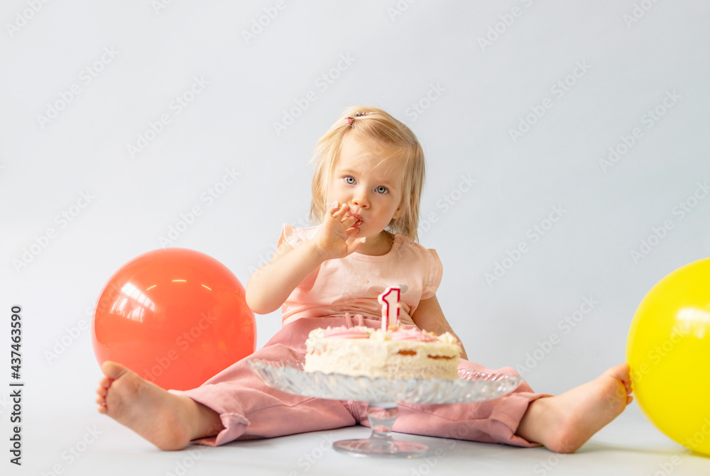 little beautiful blue-eyed girl celebrates her first birthday in the style smash a cake and she tastes her first birthday cake on a blue background with balloons little beautiful blue-eyed girl celebrates her first birthday in the style smash a cake and she tastes her first birthday cake on a blue background with balloons