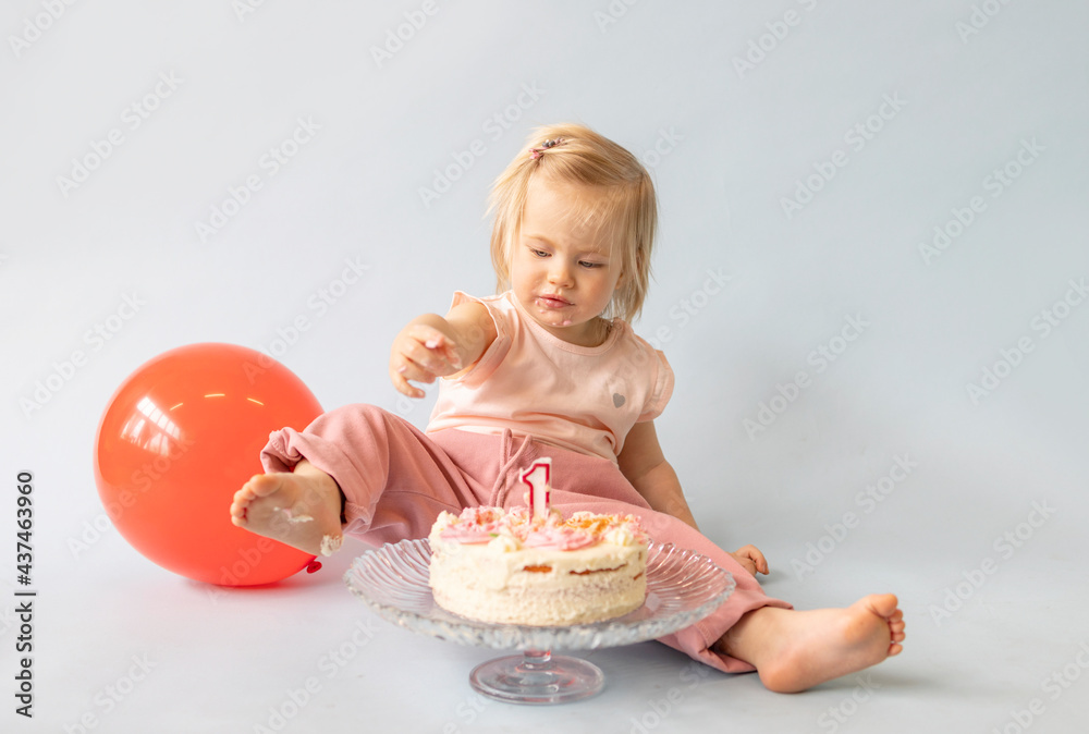 little beautiful blue-eyed girl celebrates her first birthday in the style smash a cake and she tastes her first birthday cake on a blue background with balloons little beautiful blue-eyed girl celebrates her first birthday in the style smash a cake and she tastes her first birthday cake on a blue background with balloons