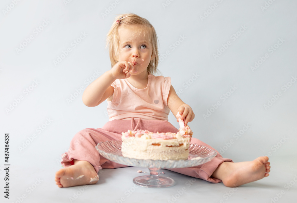 little beautiful blue-eyed girl celebrates her first birthday in the style smash a cake and she tastes her first birthday cake on a blue background little beautiful blue-eyed girl celebrates her first birthday in the style smash a cake and she tastes her first birthday cake on a blue background