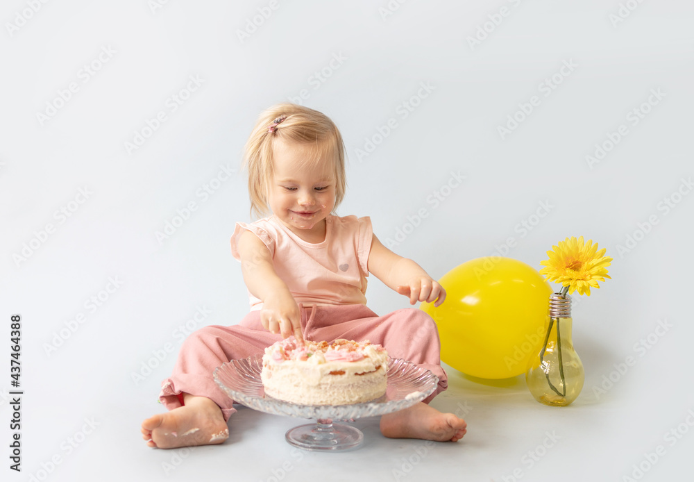 little beautiful blue-eyed girl celebrates her first birthday in the style smash a cake and she tastes her first birthday cake on a blue background with balloons little beautiful blue-eyed girl celebrates her first birthday in the style smash a cake and she tastes her first birthday cake on a blue background with balloons