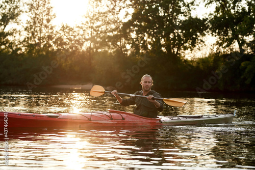 Young caucasian guy paddling kayak on a lake surrounded by peaceful nature at sunset © Svitlana