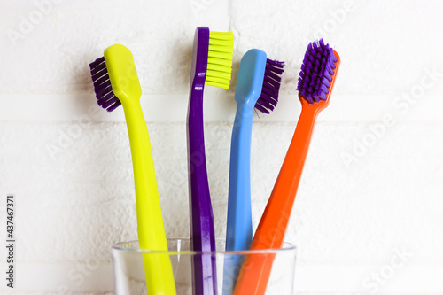 Set of plastic multicolored toothbrushes - green, blue, red, purple - in the transparent glass on a white background. Cup with four bright colorful soft toothbrushes against brick wall. Dental care.