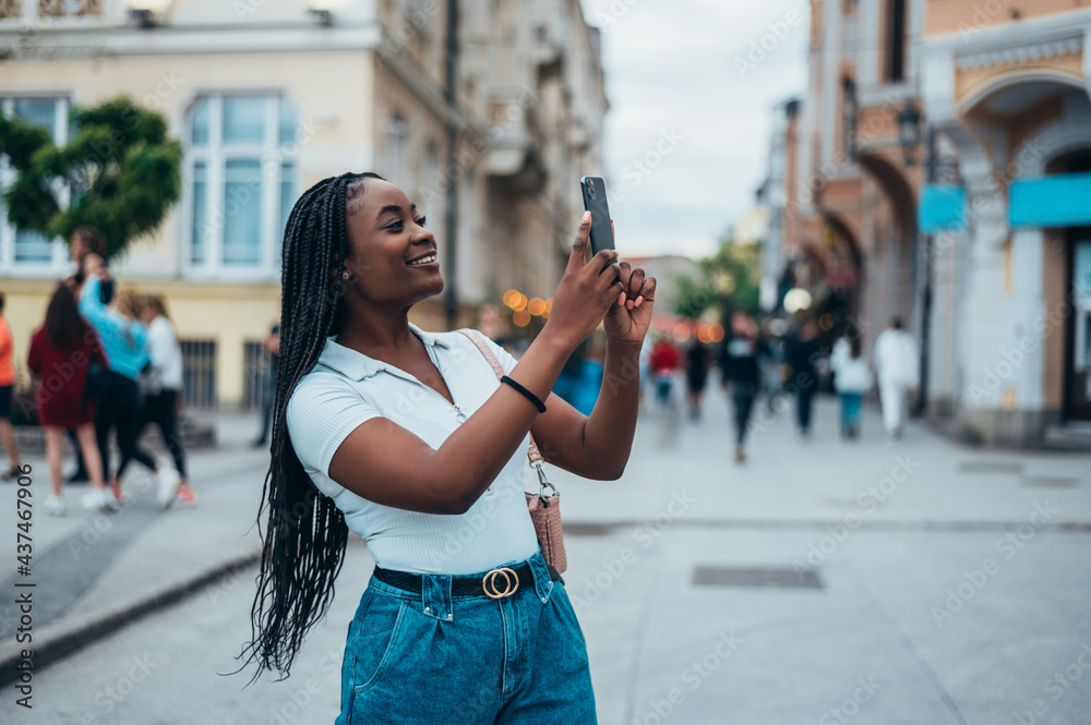 Cheerful african american woman taking selfie with her smartphone while outside in the city