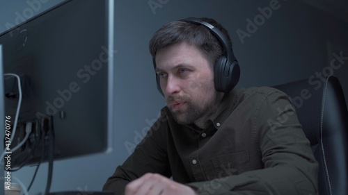 Tired male working on computer. Sad exhausted man at home office. Stressful work, stress at workplace. Software developer looks very tired during completion overtime of project, working on computer