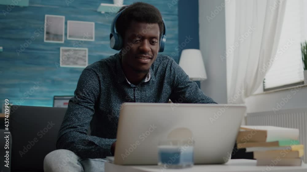 Black african american man wearing headphone, typing on laptop, using internet web online services. Remote working from home computer user using modern technology and communication devices