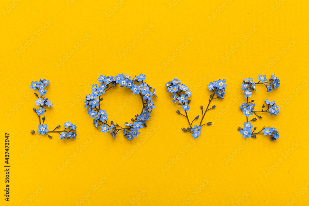 The word LOVE laid out of blue forget-me-nots flowers on a bright yellow background.
