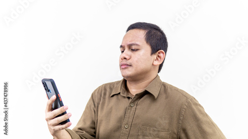 Confuse, thoughtful, doubtful and skeptical face expression of young Asian Malay man looking at the smartphone. © Aiman Khair