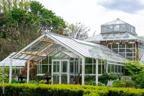Landscape view of glass greenhouse in a park with bushes, trees, growing plants and flowers.