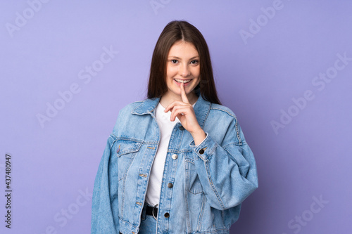 Teenager caucasian girl isolated on purple background showing a sign of silence gesture putting finger in mouth