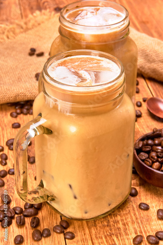iced coffee late in a glass jar on a wooden table with coffee beans and jute cloth napkins. wooden background and close up view