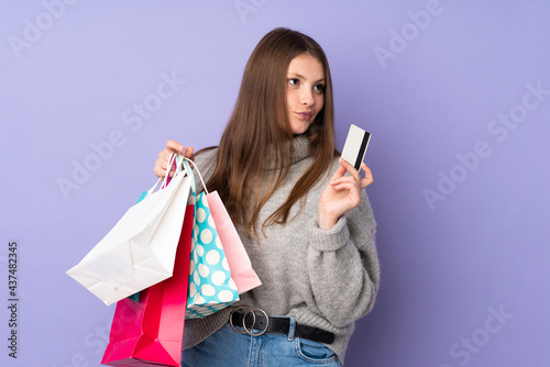 Teenager caucasian girl isolated on purple background holding shopping bags and a credit card and thinking