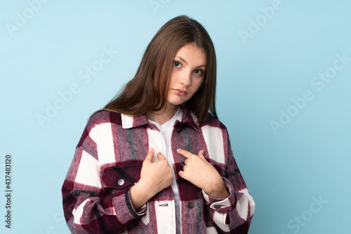 Teenager caucasian girl isolated on blue background pointing to oneself