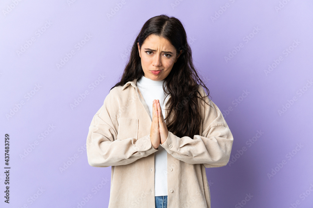 Young caucasian woman isolated on purple background keeps palm together. Person asks for something Young caucasian woman isolated on purple background keeps palm together. Person asks for something