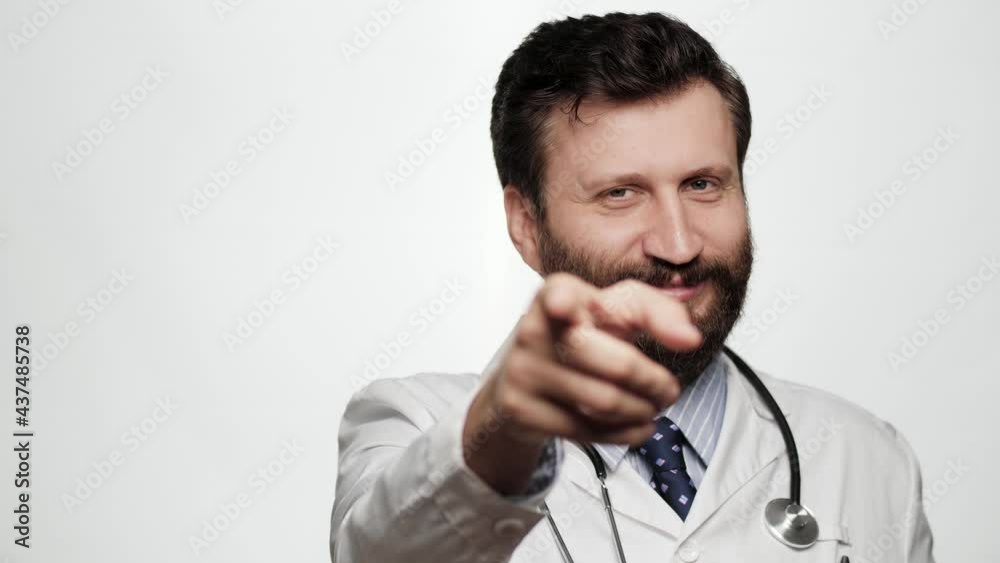 Doctor points his finger to you. Smiling kind man doctor on white background looking at camera and points his finger in camera Doctor points his finger to you. Smiling kind man doctor on white background looking at camera and points his finger in camera