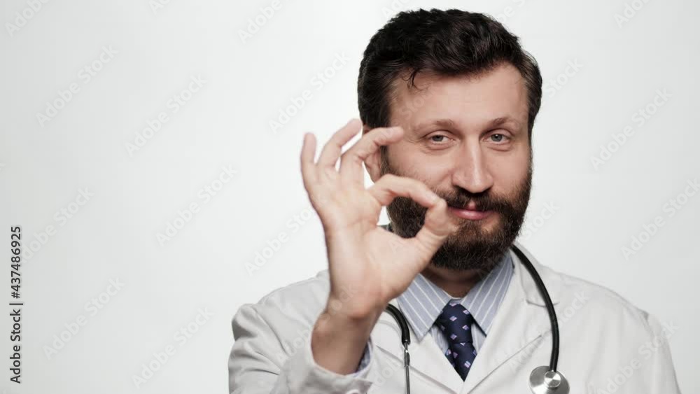 Doctor OK. Portrait of positive smiling man doctor on white background looking at camera and shows OK gesture with his fingers