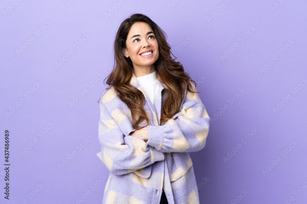 Woman over isolated purple background looking up while smiling