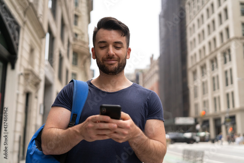 Young caucasian man on city street walking texting on cellphone