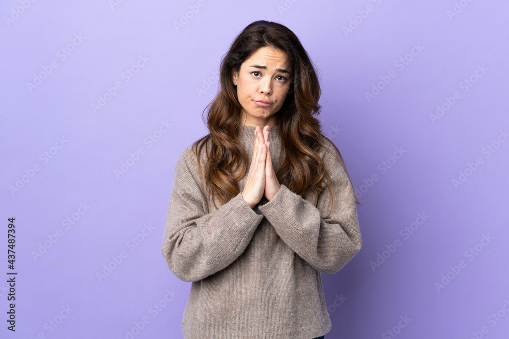 Woman over isolated purple background keeps palm together. Person asks for something Woman over isolated purple background keeps palm together. Person asks for something