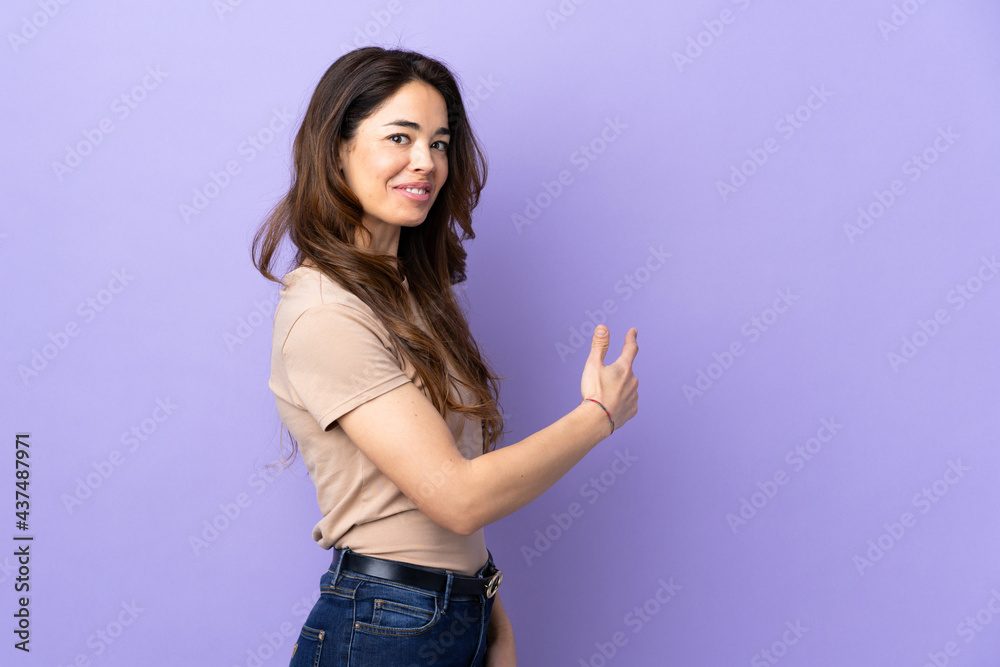 Woman over isolated purple background pointing back