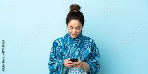 Canvastavla Woman wearing kimono over isolated background sending a message with the mobile