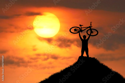 The mountain biker's silhouette lifts the bike happily that he has succeeded. from the competition On the high mountains in the evening, it is colorful. photo