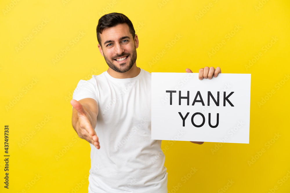Young handsome caucasian man isolated on yellow background holding a placard with text THANK YOU making a deal Young handsome caucasian man isolated on yellow background holding a placard with text THANK YOU making a deal