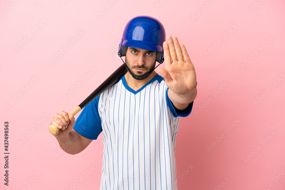 Baseball player with helmet and bat isolated on pink background making stop gesture