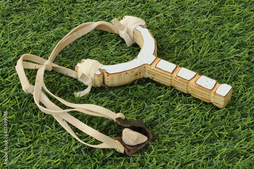 Simple homemade slingshot and stone bullet lies on a grass.