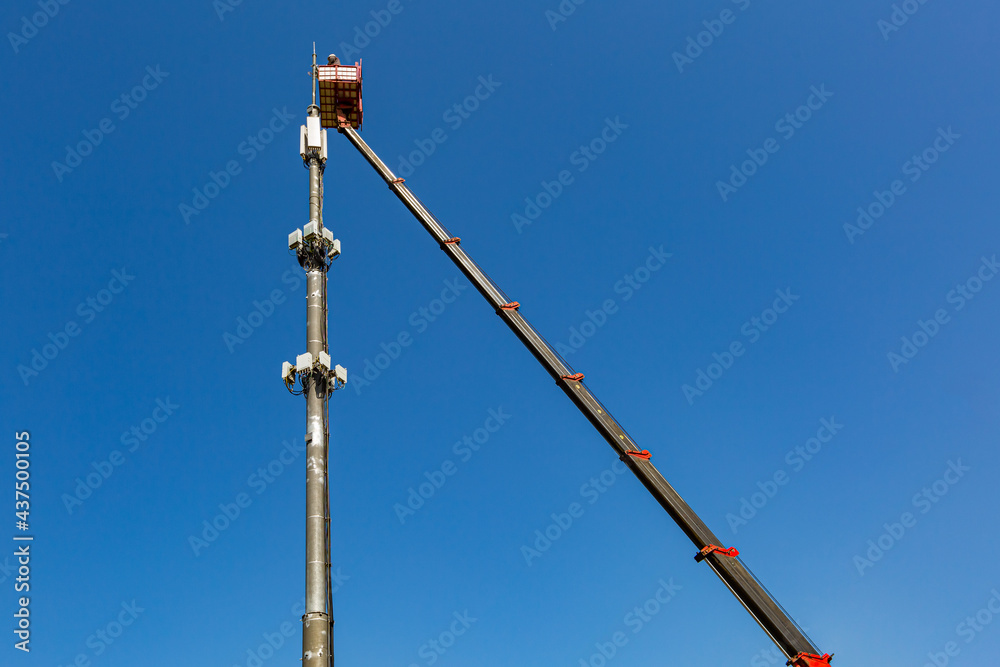 Fototapeta premium Engineer is working on thecellular phone repeater mast from An aerial work platform, also known as an aerial device, elevating work platform, cherry picker, bucket truck .