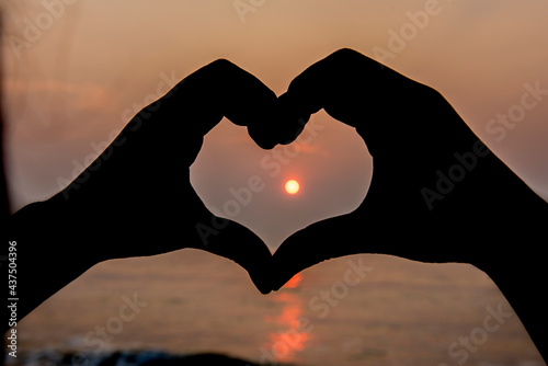 The silhouette made the heart shape from the hands at sunset.