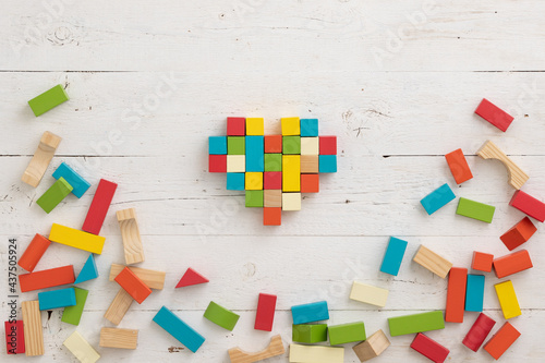 Top view of colorful wooden toy blocks on white wooden table background. The cubes are assembled in the shape of a heart. Natural materials. Healthy childhood. Learning and education concept.