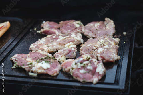 Man uses a steel ladle to turn a loaded pork neck with basil, salt, pepper and oil from one seared side to the other. Barbecue on a fierce outdoor fire. Barbecue season has begun