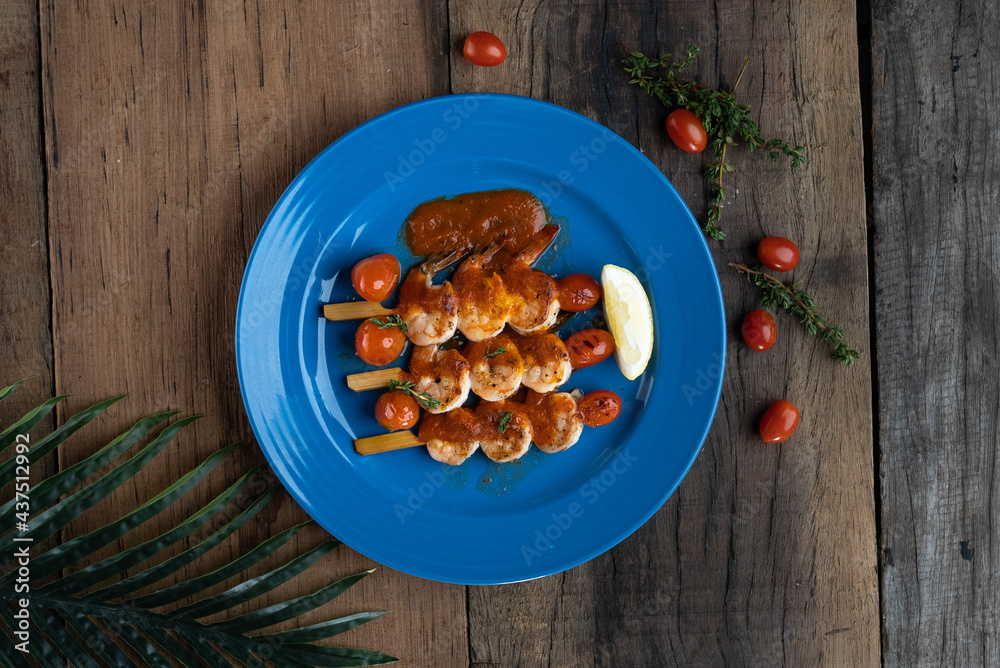 Fototapeta premium Top view of grilled marinated prawns with cherry tomato confit isolated on wooden table
